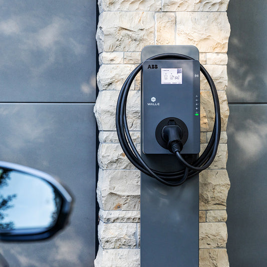 Die WALL-E Premium Wallbox auf Stele mit aufgerolltem Kabel vor einer Garage