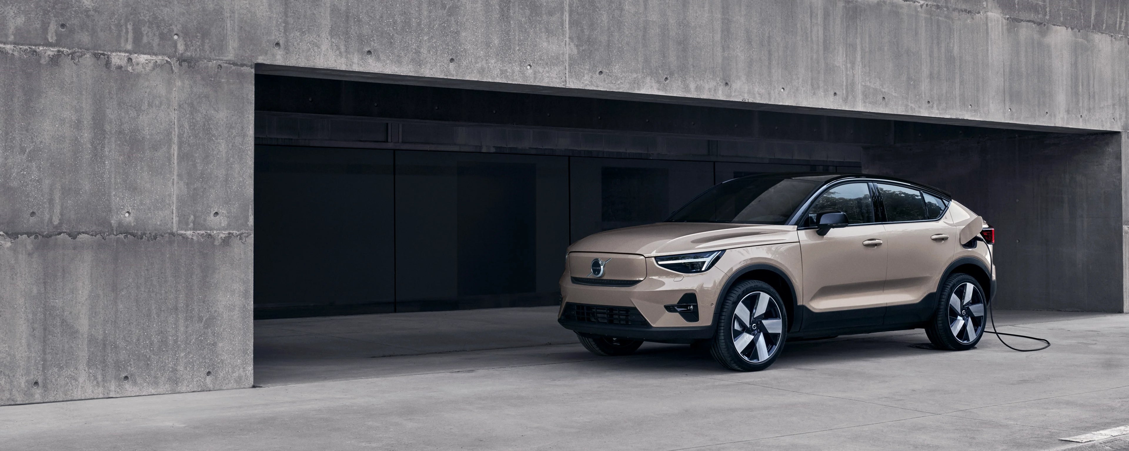 Ein Volvo EC40 mit eingestecktem Ladekabel parkt vor einem Betongebäude